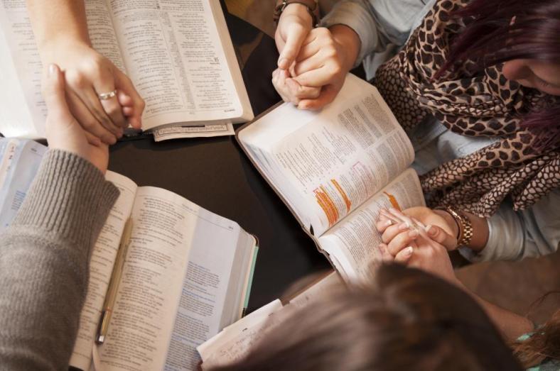 women reading bible holding hands